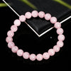 A bracelet of small, round, natural pink quartz beads is displayed on a black surface next to a dark box.