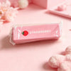 A pink strawberry shaped squishy fidget toy packaged in a clear plastic bag on a light pink surface.