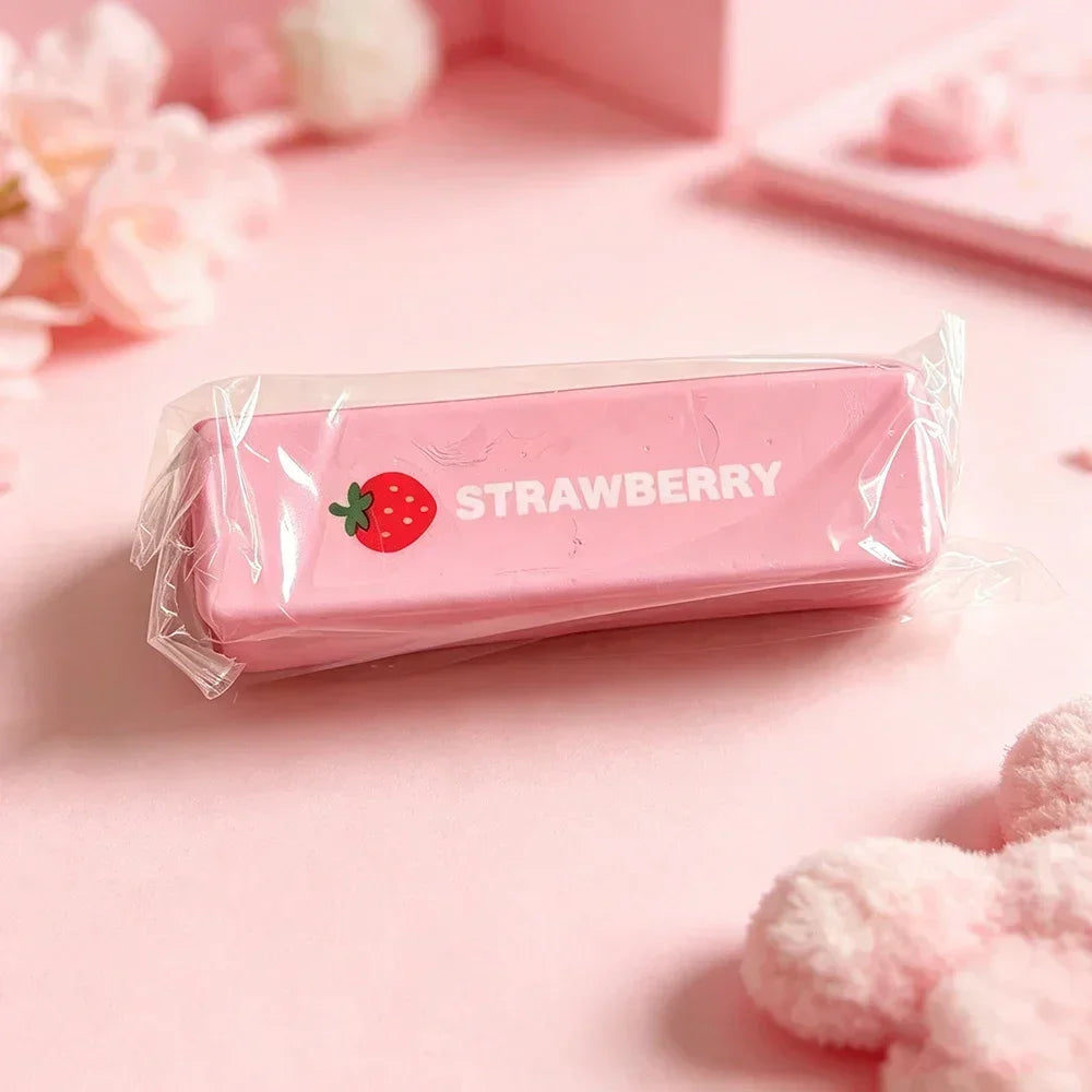 A pink strawberry shaped squishy fidget toy packaged in a clear plastic bag on a light pink surface.