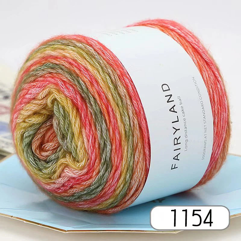 A spool of gradient rainbow yarn is shown rolled up on a light blue surface.