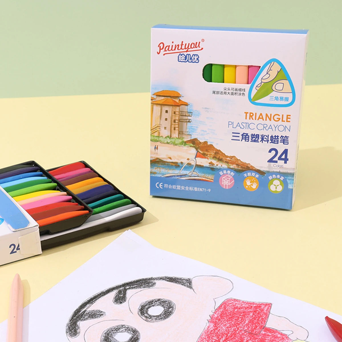 A box of Triangle Plastic Crayons with 24 colors and an ergonomic grip is shown next to a drawing.