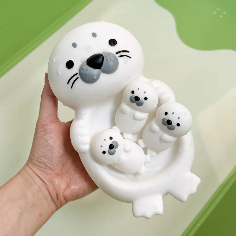 Una mano sostiene un juguete de baño de silicona blanca con forma de foca y varias focas bebé pequeñas.