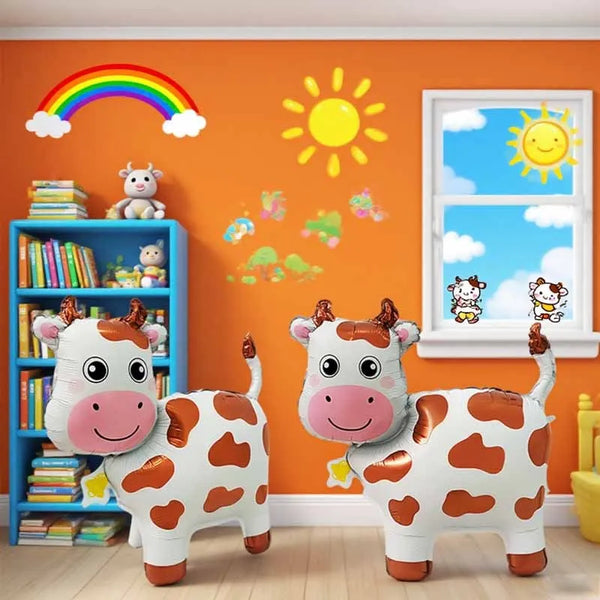A set of three 3D cartoon cow balloon decorations on a wooden floor against an orange wall with a rainbow and sun.