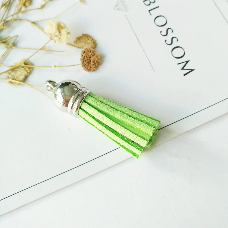 A silver tassel with bright green velvet strands rests on a white paper with the word BLOSSOM visible.
