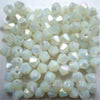 A pile of small, faceted glass bicone beads in translucent white and pale iridescent colors.