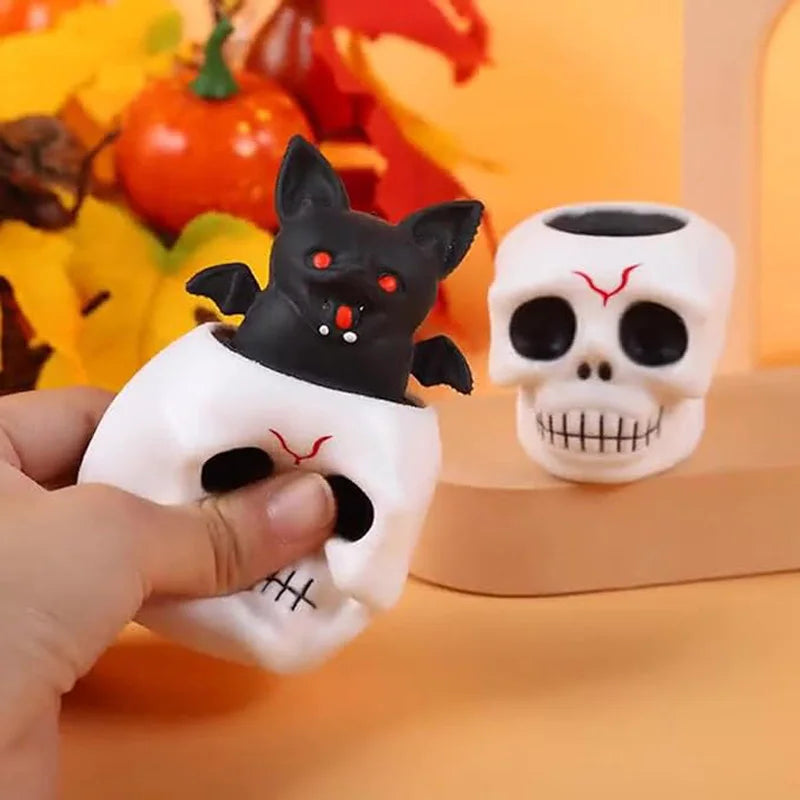 A hand holds a black cat and white skull squeeze stress ball toy against an orange background.