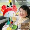 A baby is holding a crab-themed rattle and teether toy with hanging straps in a car seat.