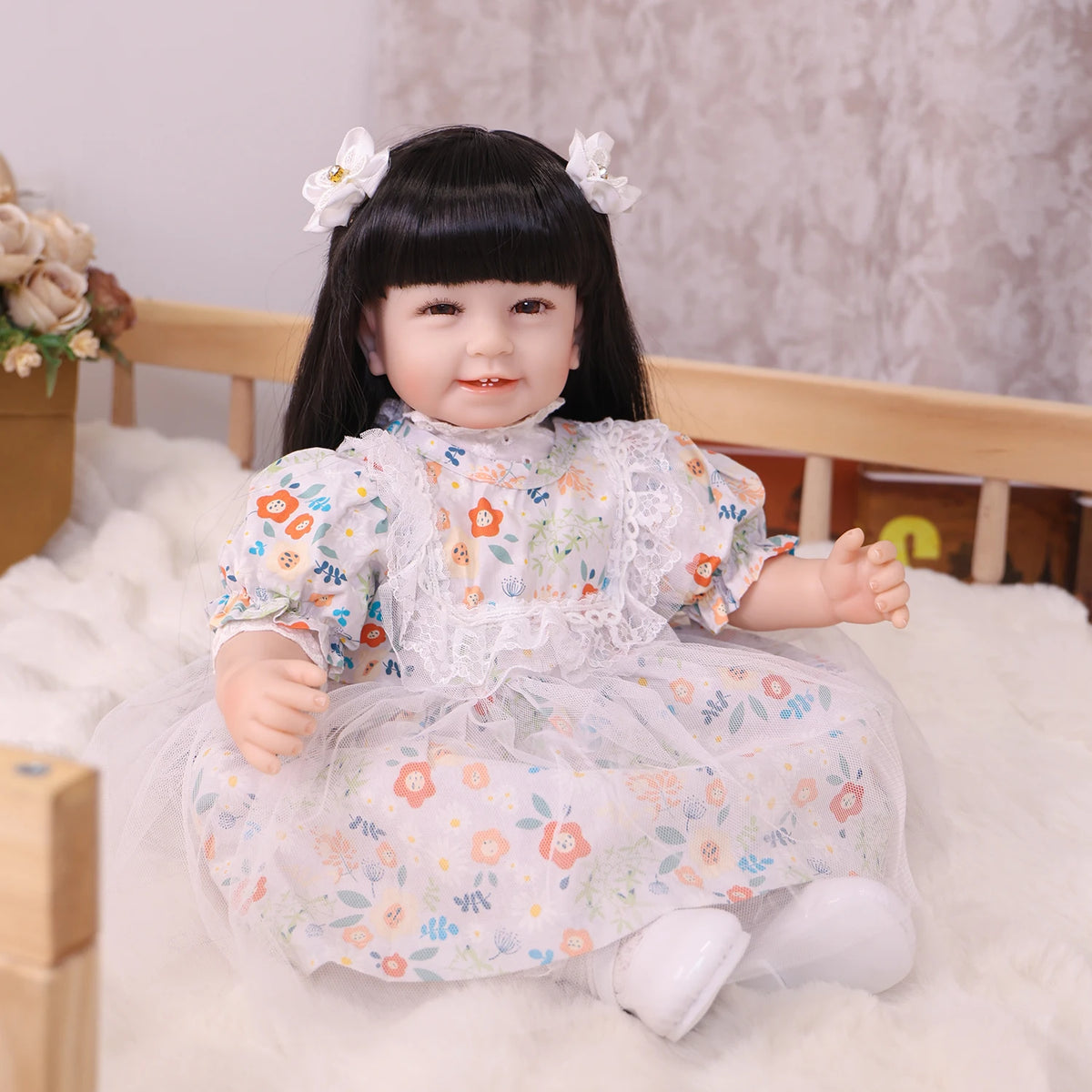 A baby doll with black hair and a floral dress is sitting on white fluffy material.