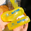 A hand holds a yellow butter squishy stress relief toy labeled 4oz net wt 113g