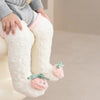 A close-up of a baby wearing white fuzzy knee-high socks with pink accents and a green fruit design.