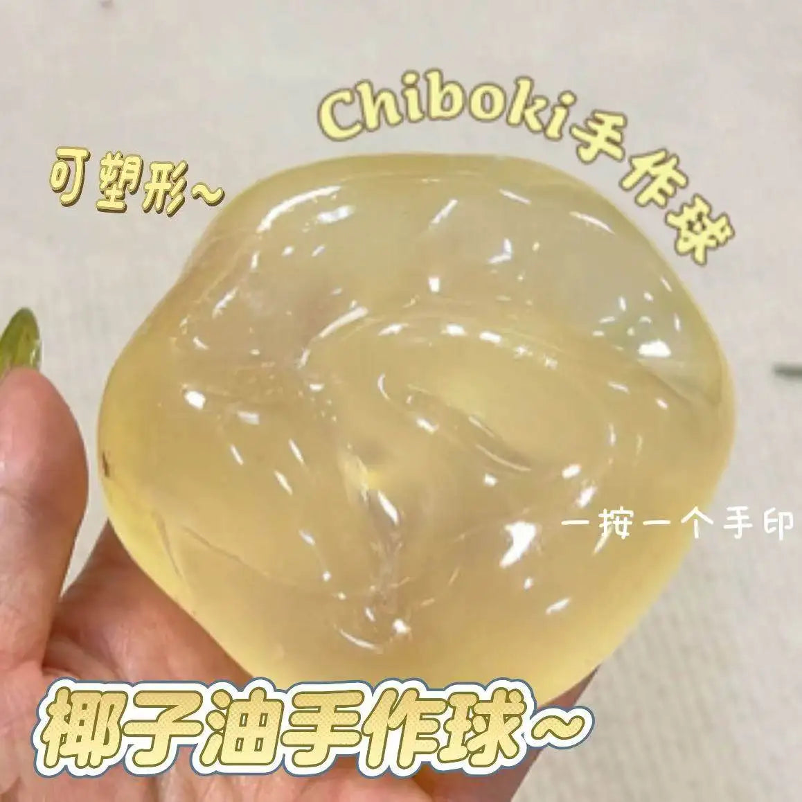 A hand holds a translucent yellow handmade slow rebound squeeze ball made from coconut oil.