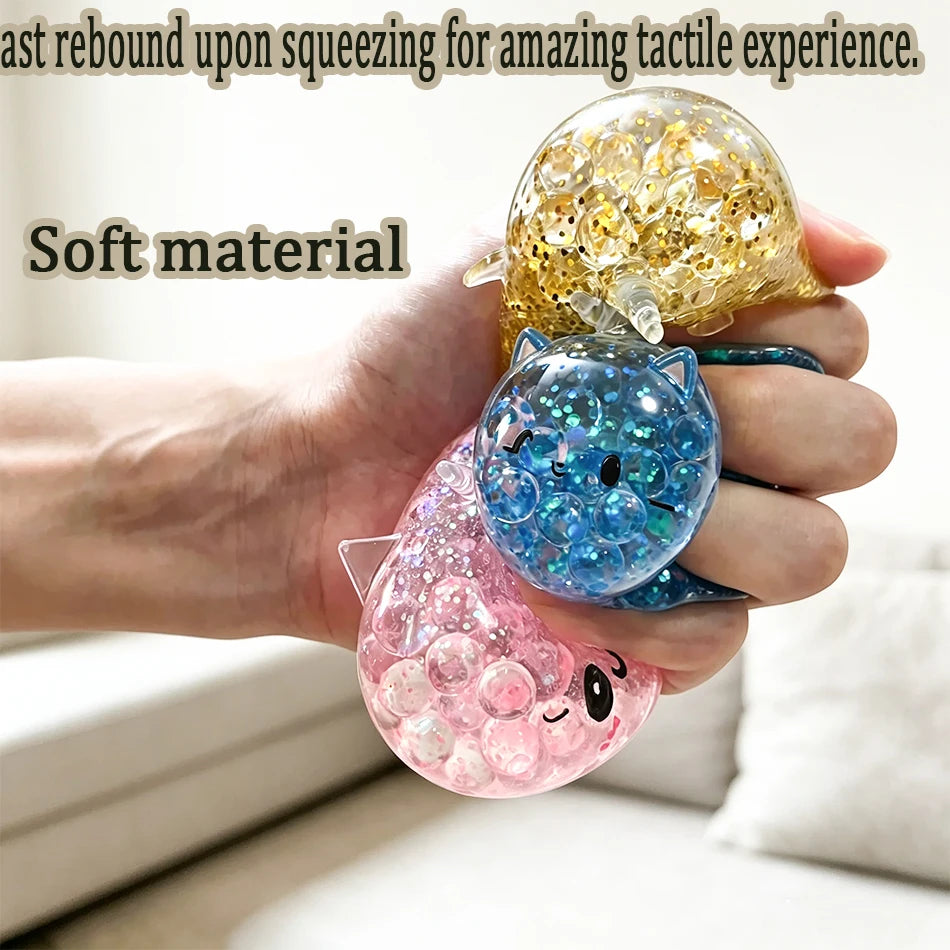 A hand holds a soft, glittery unicorn bun squishy toy with a cat face and a golden glitter ball.