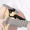 A hand holds an adjustable guitar phone holder device attached to the neck of a guitar.