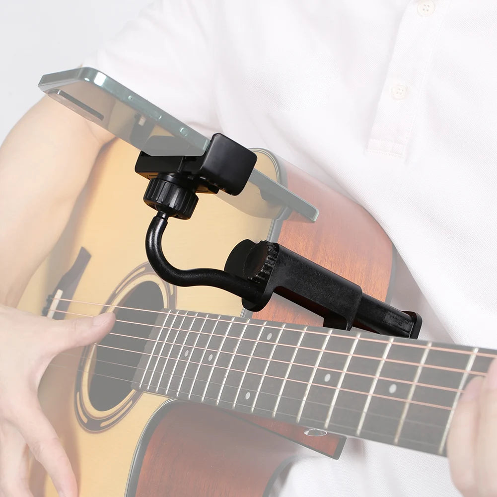 A hand holds an adjustable guitar phone holder device attached to the neck of a guitar.