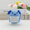 A handwoven blue crochet pencil ornament with a smiling face sits in front of a box of pencils and flowers.