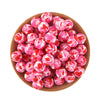 A pile of pink and red silicone beads for jewelry making in a wooden bowl.