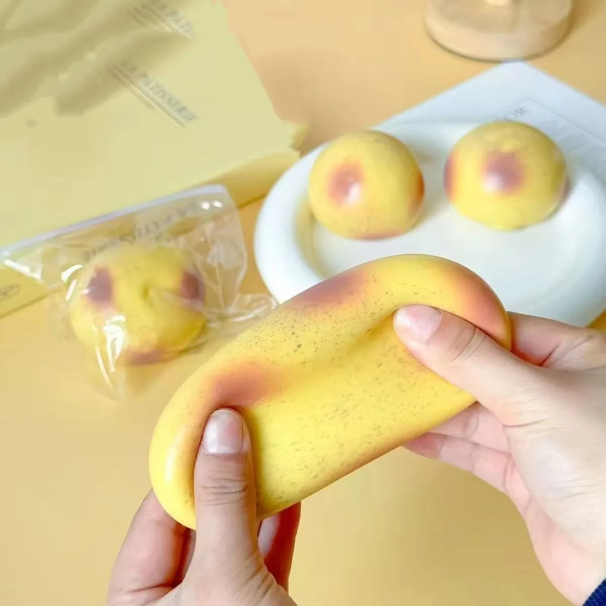 Hands hold a yellow squishy potato fidget toy next to two similar toys on a white plate.