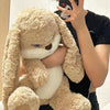 A person is holding a giant soft plush rabbit toy with light brown fur and white accents.