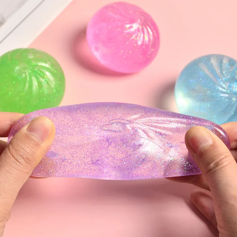 Hands hold a purple glitter squishy bun fidget toy next to colorful plastic balls.