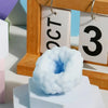 A light blue, squishy stress relief ball is displayed in front of a wooden frame with month and day tags.