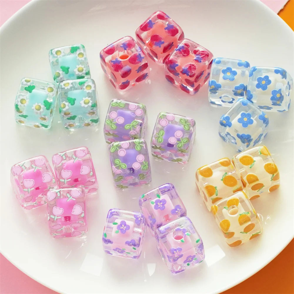 A collection of colorful floral square resin beads in pink, purple, and blue are displayed on a white plate.