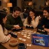 A group of people playing a game of Rummikub using black racks and tiles on a wooden table.