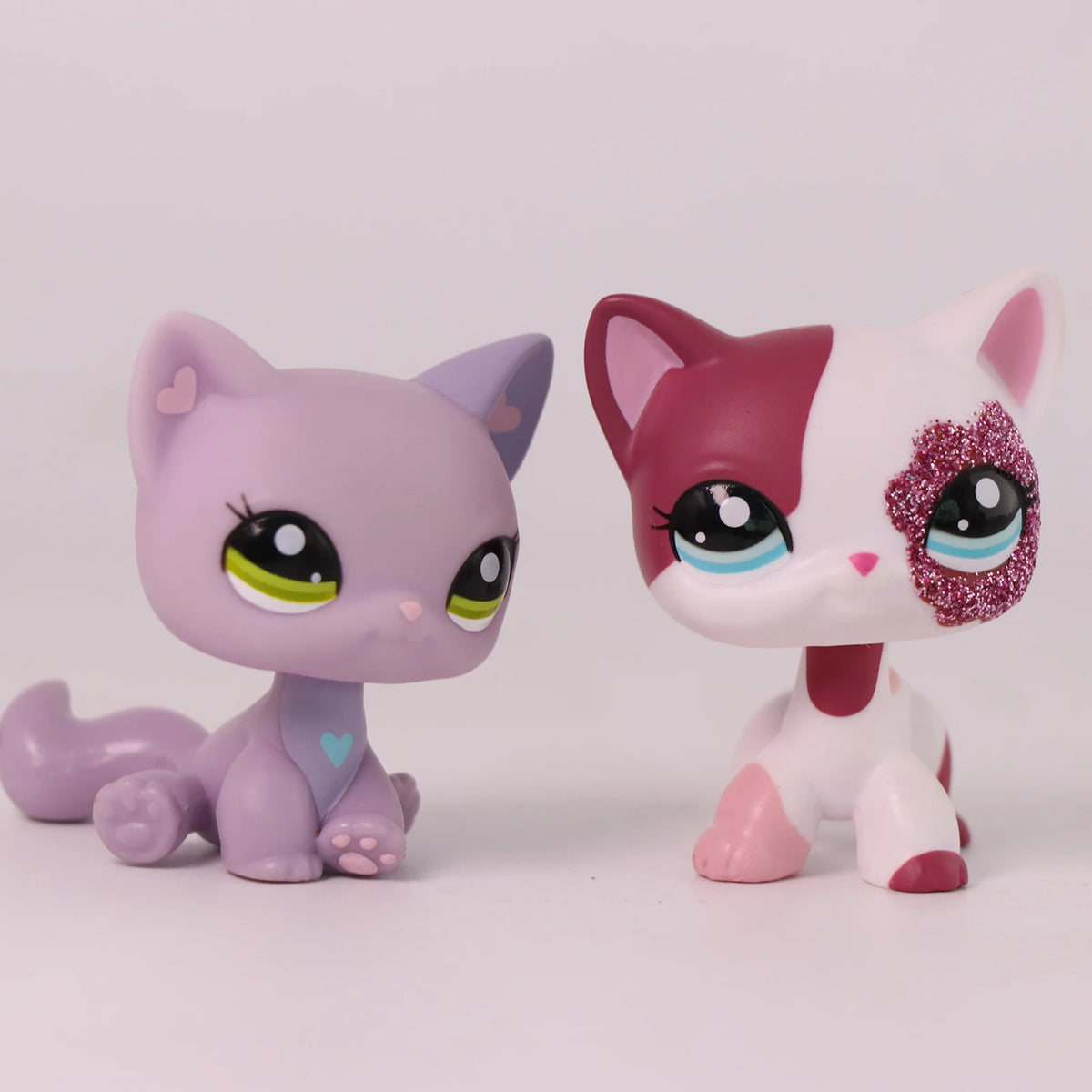 A pair of Shorthair Cat Bobble Head figurines, one purple and one pink with white markings.