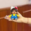 A hand is holding a Monchhichi plush monkey with a white and red bow on its head.