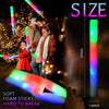 A hand holds a glowing foam LED stick next to people playing with similar glow sticks in a festive setting.