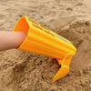An orange kids excavator digging toy is shown in the palm of a hand, resting on sand.