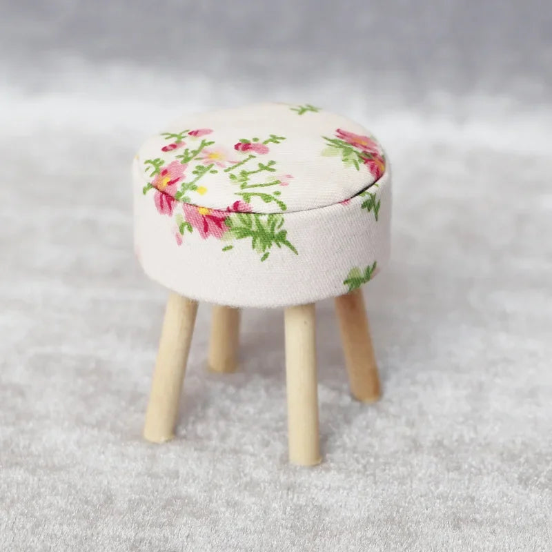 A miniature sofa and pillow set for a dollhouse featuring a light cream fabric with pink and green floral embroidery.