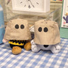 A tan plush keychain charm shaped like a dog with black eyes and a striped collar sitting on a blue checkered cloth.