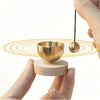 A hand holds a small brass singing bowl resting on a wooden base with a mallet above it.