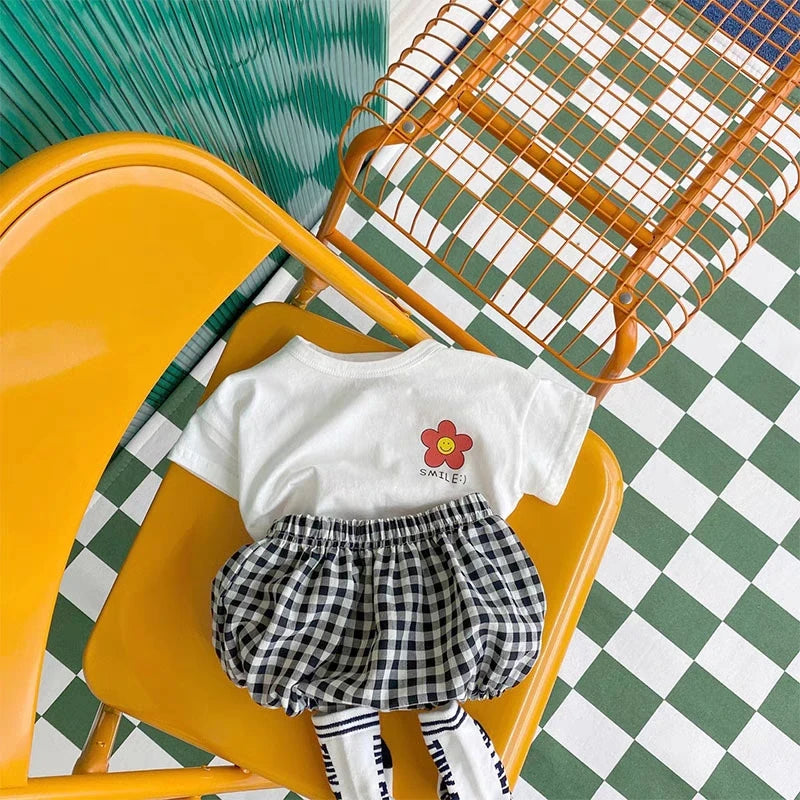 A white t-shirt with a smiling flower graphic and black and white checkered shorts displayed on a yellow chair.