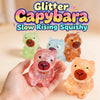 A hand holds a pink glitter capybara slow rising squishy toy next to other colorful squishies.