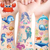 A collection of colorful glitter mermaid and underwater sea creature temporary tattoos on a person's arm.