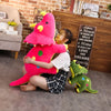 A young girl is hugging a large pink dinosaur plush toy in front of a wooden bookshelf and brick wall.