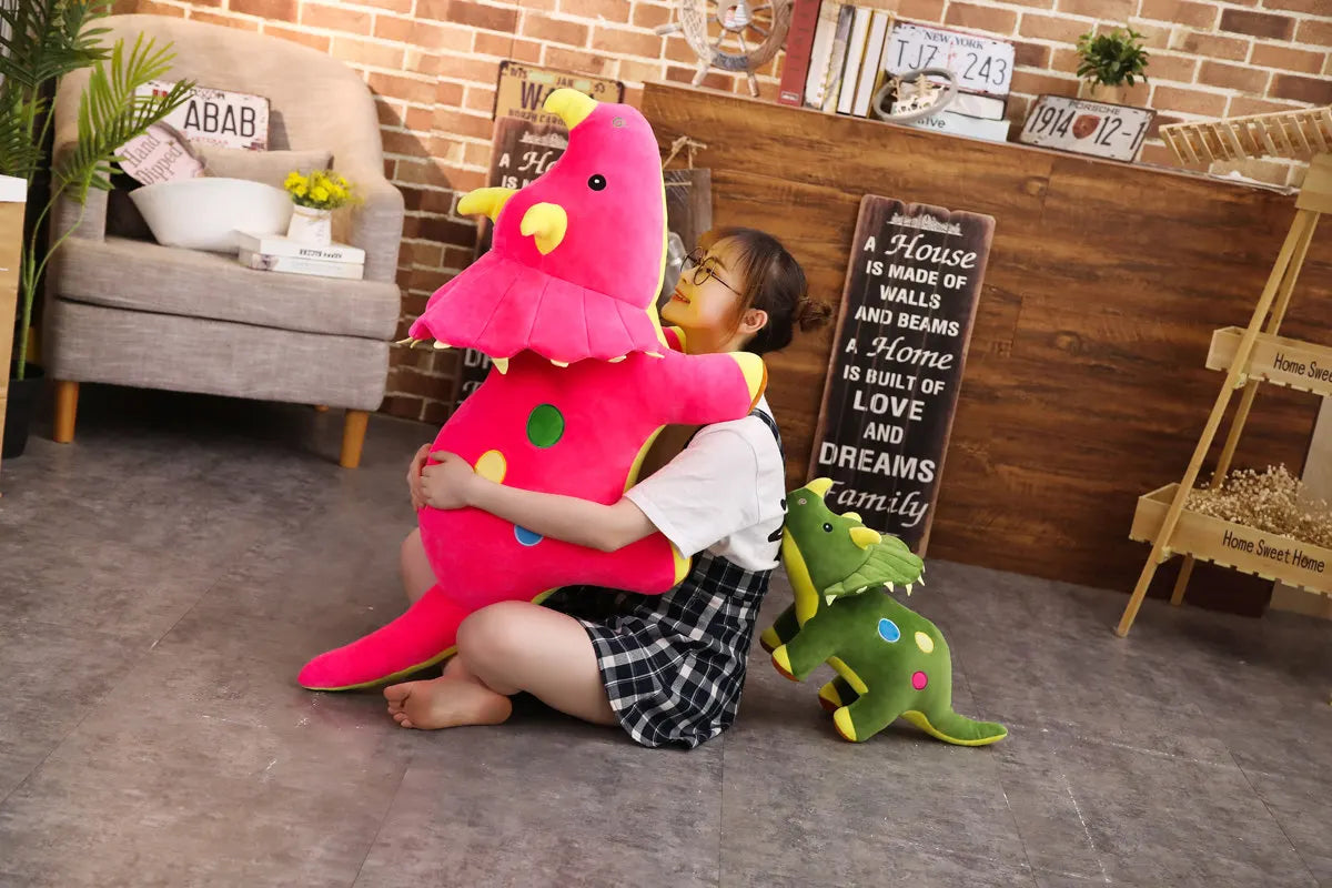 A young girl is hugging a large pink dinosaur plush toy in front of a wooden bookshelf and brick wall.