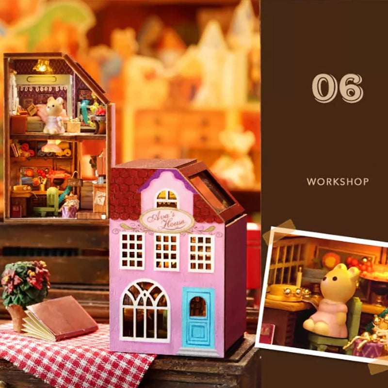 A pink and blue wooden miniature dollhouse kit with a pitched roof is displayed next to a blurred background of other toys.