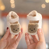 A pair of white bear soft sole first walker shoes for babies being held by a person.