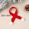 A red knitted Christmas hat or scarf with white pom-poms, displayed on a light background next to pine cones and evergreen br