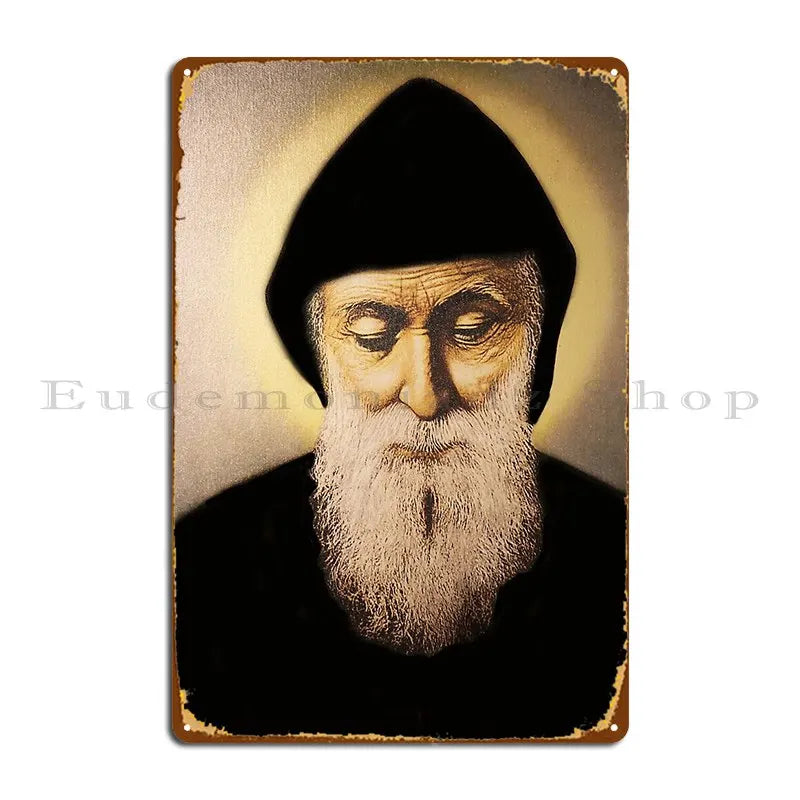 A vintage metal wall sign featuring a portrait of Saint Charbel with a beard against a dark background.