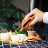 An orange silicone pretend play tea set with a spout is being held over a collection of small cups and saucers.