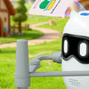 A white robot is using a stylus to draw a cactus on paper in a grassy outdoor setting.