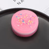 A pink squishy stress relief toy with colorful sprinkles resting on a dark gray surface.