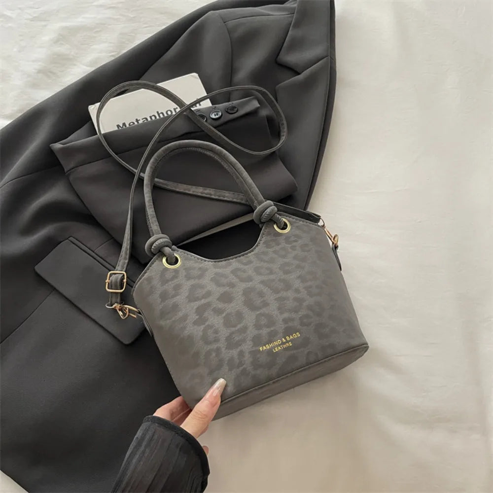 A gray floral canvas tote bag with leather straps is shown resting on a dark gray blazer.