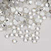 A close-up view of clear glass crystal flatback rhinestones in various sizes and shapes scattered on a white surface.