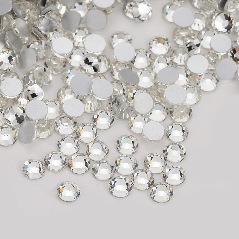 A close-up view of clear glass crystal flatback rhinestones in various sizes and shapes scattered on a white surface.