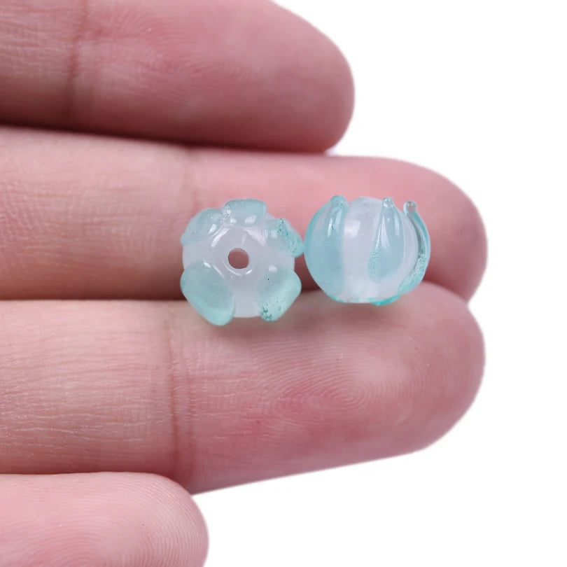 A small, translucent pale blue glass charm shaped like a lily of the valley flower resting on a person's finger.