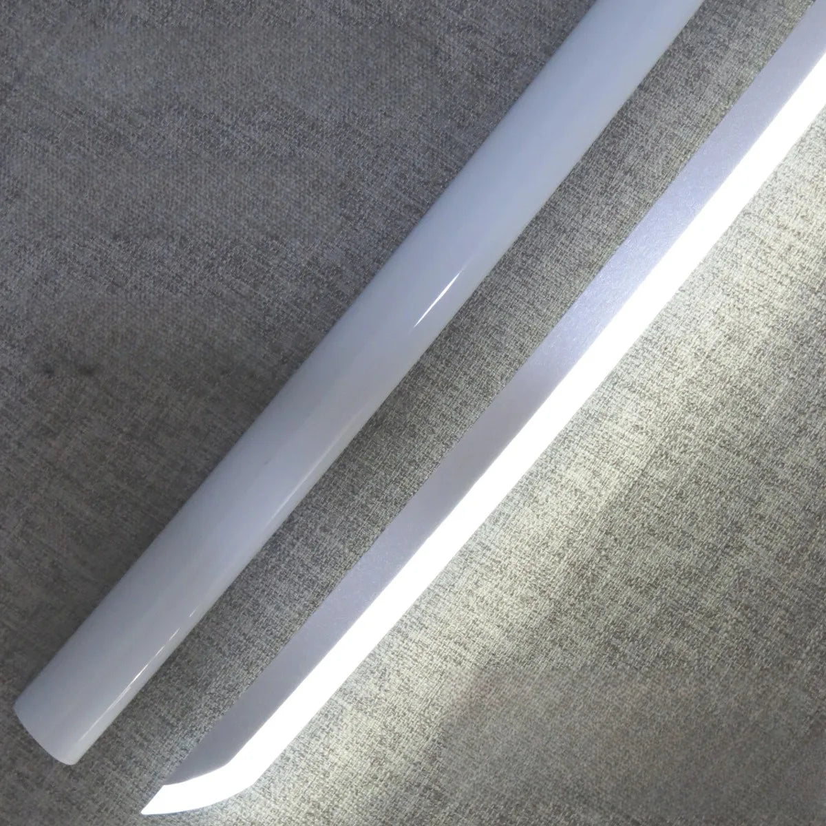 A white luminous anime katana prop with an LED blade is shown angled against a textured wall.